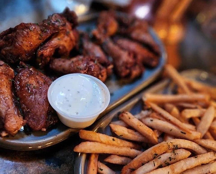 A platter of crispy chicken wings accompanied by a small cup of dipping sauce and a generous serving of seasoned fries.