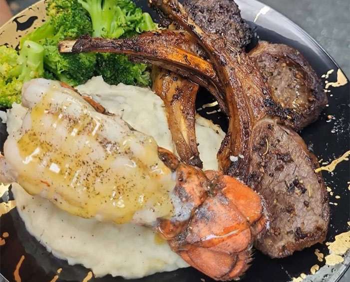 A gourmet plate featuring grilled lamb chops, creamy mashed potatoes, a lobster tail with butter, and steamed broccoli.